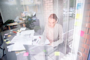Genç dalgın iş arkadaşı, ahşap masada otururken güneşli bir iş yerinde çalışıyor. Adam dizüstü bilgisayardaki belgeyi analiz ediyor. Bulanık geçmişi..