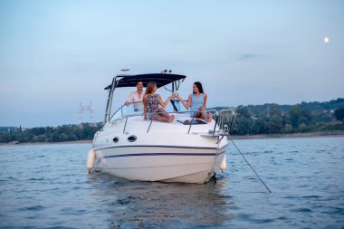 İki kız ve bir adam bir teknede eğleniyor, dinleniyorlar.