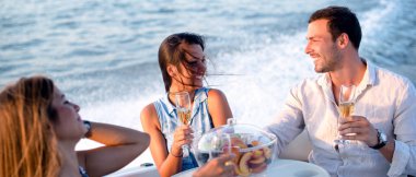 İki kız ve bir adam teknede şarap içiyorlar.