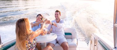 İki kız ve bir adam teknede şarap içiyorlar.