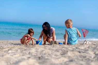 Anne ve iki çocuk sahilde kumdan kale inşa ediyorlar.