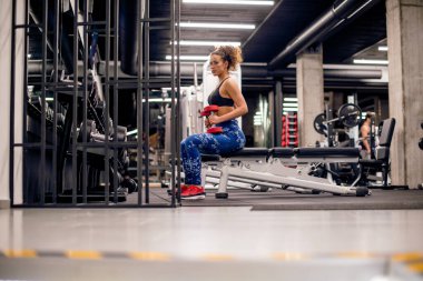 Çekici genç bayan spor salonunda küçük kırmızı ağırlıklarla antrenman yapıyor.