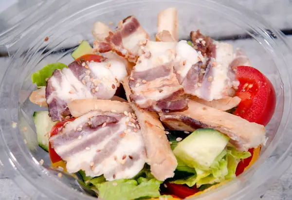 Yaprak sebzeli salata, domates ve et gri arka planda açık kasede..