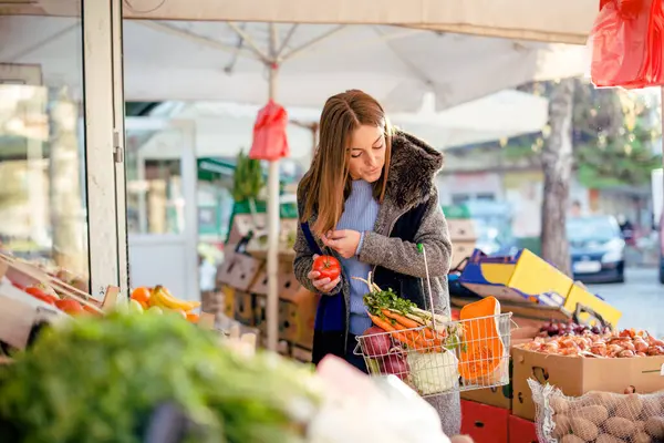 Genç kadın domates alıyor, lahana, balkabağı, havuç ve havuç dolu sepete domates koyuyor..