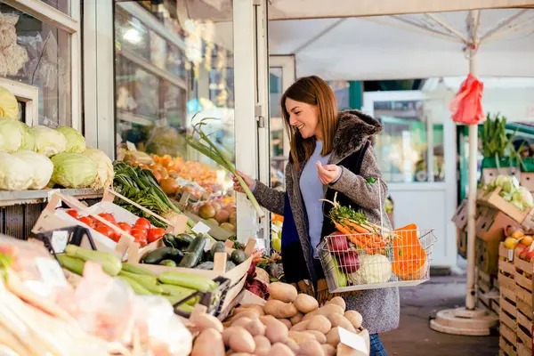 Çiftçi pazarından sebze toplayan gülümseyen kadın elinde taze sebzelerle dolu bir sepet tutuyor..