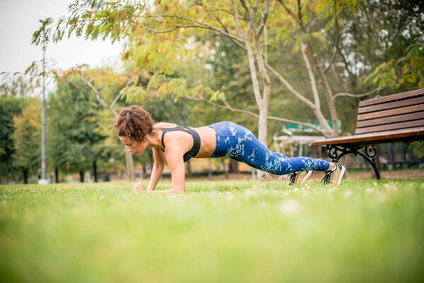Young woman doing plank exercises in public park, side view.