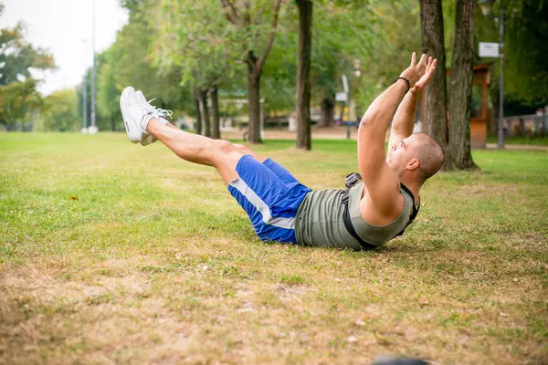 Parkta egzersiz yapan yakışıklı bir adam, elleri ve bacakları havada..