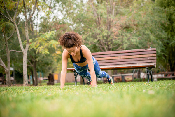 Young woman doing push-ups on grass in public park.