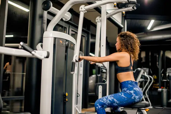 Genç ve çekici bir kadın spor salonunda makineyle çalışıyor.