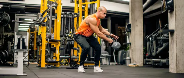 Spor salonundaki adam kettlebell ile salıncak egzersizi yapıyor.