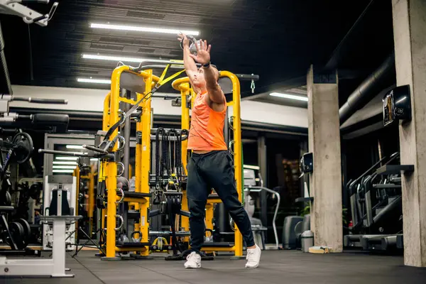 Spor salonundaki adam kettlebell ile salıncak egzersizi yapıyor.