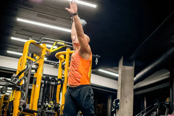 Spor salonundaki adam kettlebell ile salıncak egzersizi yapıyor.