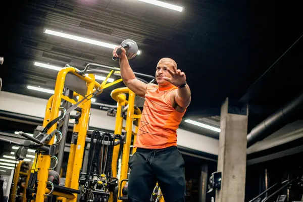 Spor salonundaki adam kettlebell ile salıncak egzersizi yapıyor.