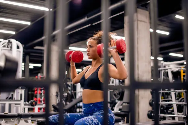 Çekici genç bayan spor salonunda küçük kırmızı ağırlıklarla antrenman yapıyor.