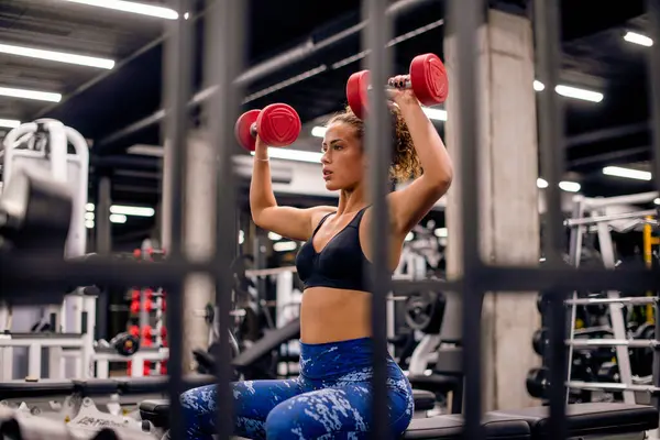 Çekici genç bayan spor salonunda küçük kırmızı ağırlıklarla antrenman yapıyor.