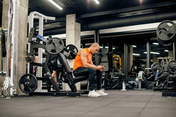 Çekici genç adam spor salonunda telefonuna bakıyor.