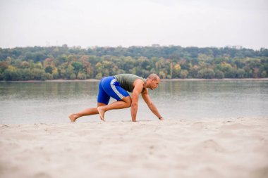 Yakışıklı sporcu plajda egzersiz yapıyor, bacakları için egzersiz yapıyor..