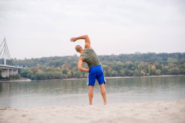 Ahlete plajda çalışıyor, yalınayak spor şortu giyiyor ve kolsuz..