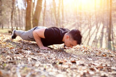Şınav çeken genç bir adam, doğada egzersiz yapıyor.