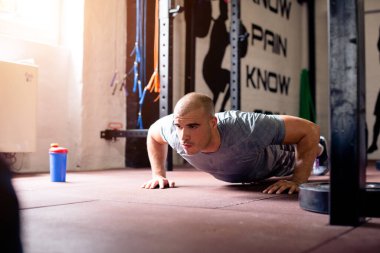 Spor salonundaki kaslı adam şınav çekiyor.