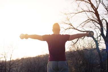 Adam doğada çalışıyor, ağırlık kaldırıyor, arkadan bakıyor.