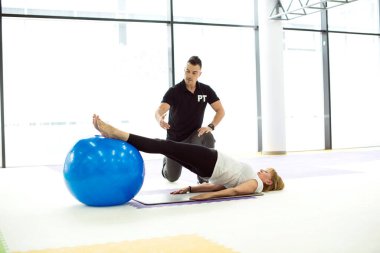 Kıdemli kadın koçla egzersiz yapıyor, top oynuyor.