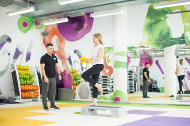 Kıdemli kadın kişisel antrenörünün yardımıyla ağırlık eğitimi alıyor.