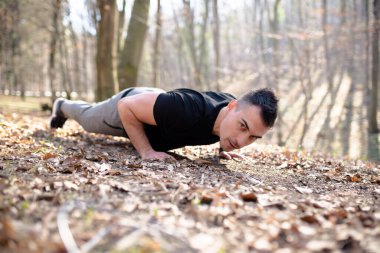 Güçlü genç adam şınav çekiyor, doğada egzersiz yapıyor.