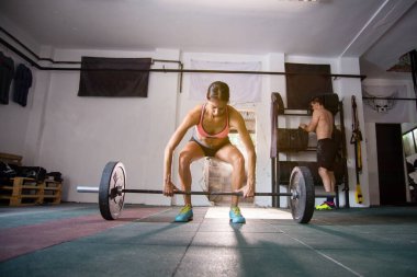 Güçlü genç bayan spor salonunda ağırlık kaldırmaya hazırlanıyor.
