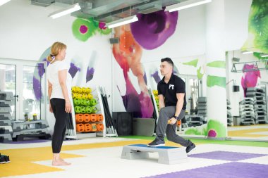 Eğitmen yaşlı kadına ağırlık egzersizi gösteriyor.