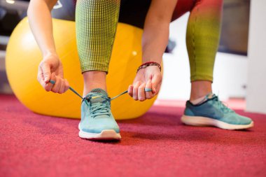 Spor salonunda ayakkabı bağlayan, spor salonunda oturan bir kadın.