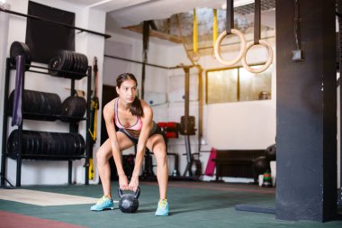 Spor salonunda çaydanlık çanlarıyla çalışan genç bir kadın.