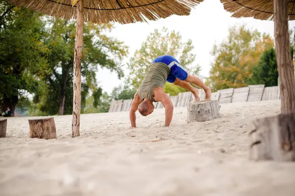 Erkek sporcu plajda amuda kalkmaya hazırlanıyor. Düşük açılı..