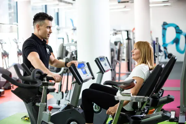 Özel antrenör onu motive ederken kıdemli bayan bisiklet egzersizi yapıyor.