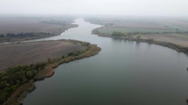 Drone, Krivaja Gölü 'nü sisli sonbahar gününde ağaçlarla çevrili halde yakalıyor.