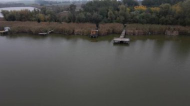 Drone, Sırbistan 'daki Zobnatica Gölü kıyısındaki rıhtım ve kulübelerin üzerinden uçuyor