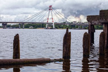 Beyaz kabloyla nehir boyunca köprü, harap olmuş ahşap iskele, kara bulutlar, nehir akıntısı.