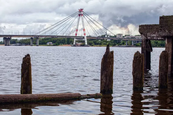 Beyaz kabloyla nehir boyunca köprü, harap olmuş ahşap iskele, kara bulutlar, nehir akıntısı.