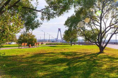 Parkta yeşil çimen, arkada köprü ve nehir.