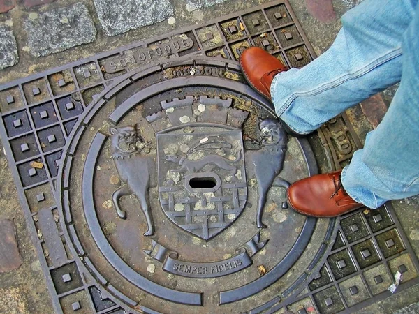 Rögar kapağında belediye arması, kot pantolon ve deri ayakkabılarla görünen bacaklar. Gönderilen Malo, Fransa
