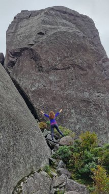 Bir dağcı dramatik bir gökyüzü altında büyük bir kaya oluşumuna yükselir, ruhlarını ve cesaretlerini gösterir.