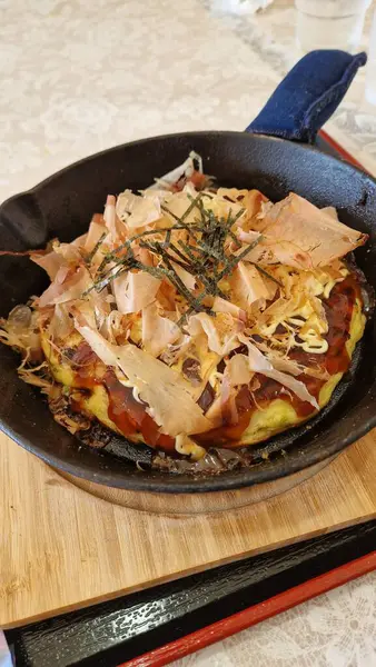 Ağız sulandıran bir okonomiyaki üzerine bonito gevreği ve yosun dökülmüş demir bir tabakta cızırdıyordu..