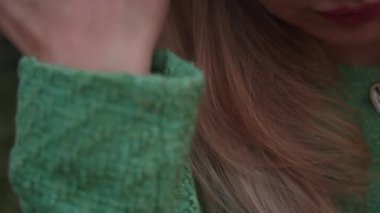 Kadın elini saçlarının arasından omzunun üstünden geçiriyor. Yeşil takım elbiseli sarışın bir kadın elini omzunda ve saçında gezdiriyor..
