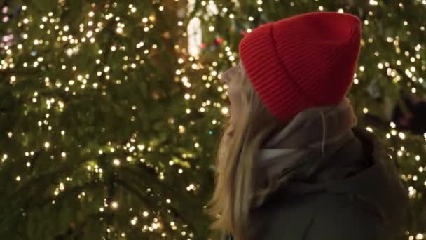 一个快乐的女孩抬头看着圣诞树 然后直接对着摄像机 — 图库视频影像