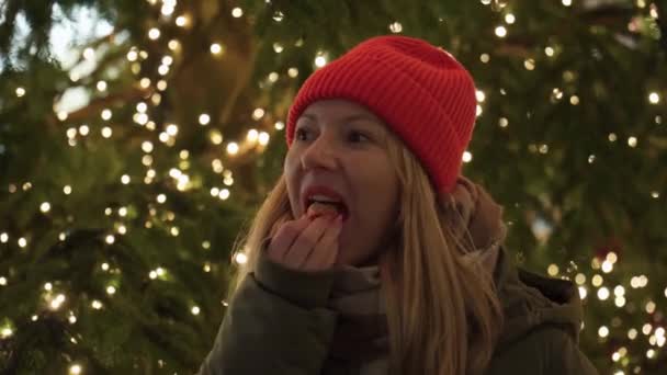 Mädchen Essen Eine Mandarine Der Nähe Des Weihnachtsbaums Roter Hut — Stockvideo