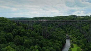 Mungstener Brucke Germanys 'in soldan sağa uçan en yüksek demiryolu köprüsünün geniş açılı görüntüsü. Yolcu treni Wupper Nehri, ağaçlar ve aşağıdaki park alanlarıyla köprüden geçer. Parçalı bulutlu bir günde 4K 'da yakalandı.