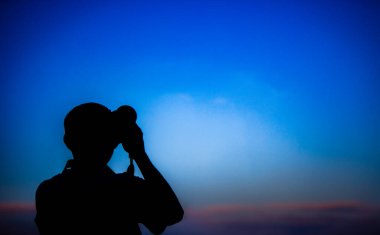 Öğrenci fotoğrafçısının silueti alacakaranlıkta ateş ediyor.