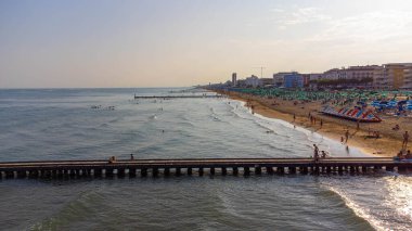 Jesolo Lido plajı gün batımında İHA 'dan. Deniz dalgalarıyla ahşap yollar, plaj tatillerinde turistlerle dolu plajlar. Plajlar ve Akdeniz, İtalya 'nın Adriyatik Denizi, yazın turizm beldesi