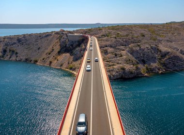 Güneşli bir günde yol fotoğrafı rehberi. Denizin üzerindeki bir köprüde arabalar, araba yolculuğu geçmişi. Maslenica Köprüsü.