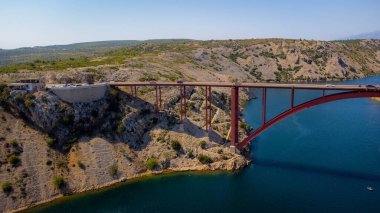 Doğal kıyı manzarasının ortasında ulaşım ve sürdürülebilirlik için inşaat. İki zıt parçayı birbirine bağlamak için deniz üzerindeki köprü. Maslenica Köprüsü, Hırvatistan.